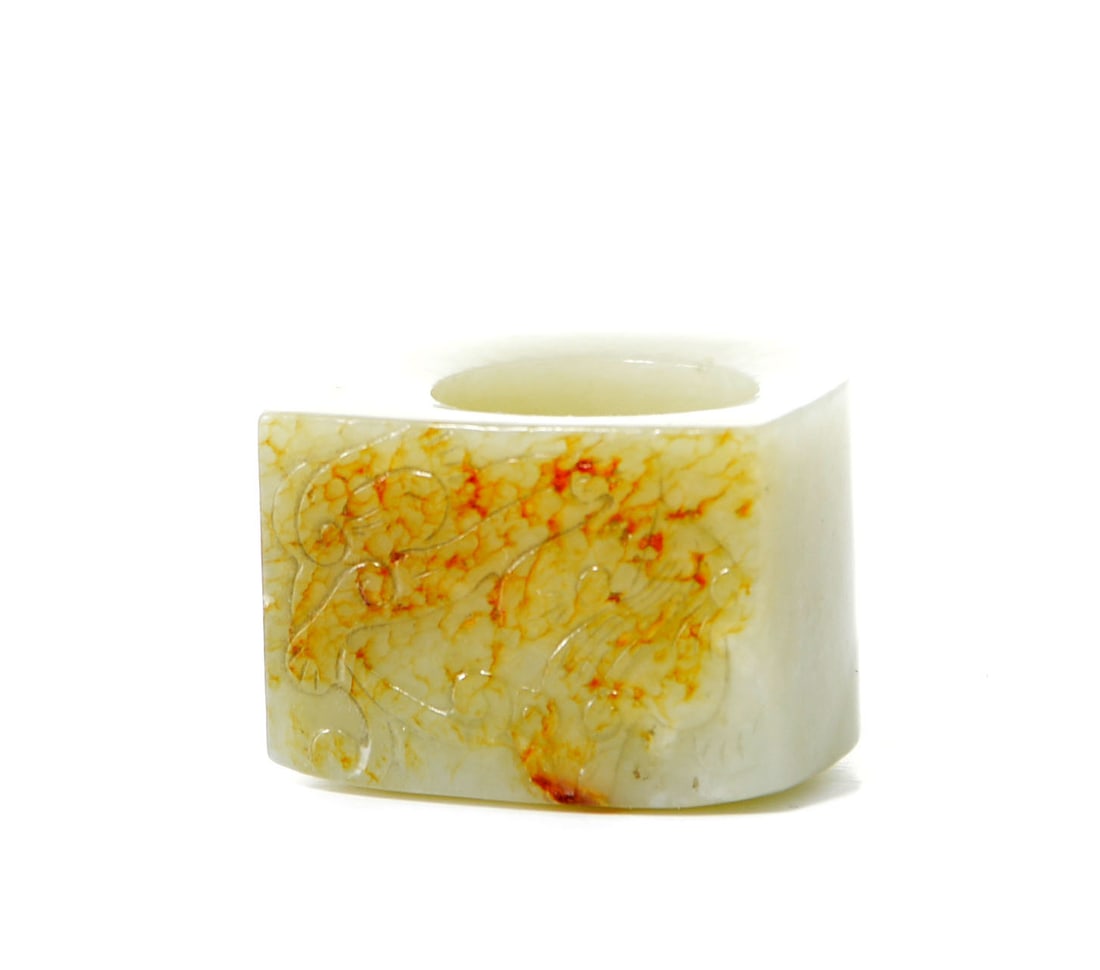 Chinese Carved Jade Archer's Ring: Of gently waisted cylindrical form, the pale celadon stone is carved in low relief with a sinuous dragon amid cloud scrolls. The stone is attractively suffused with russet and amber inclusions, with n