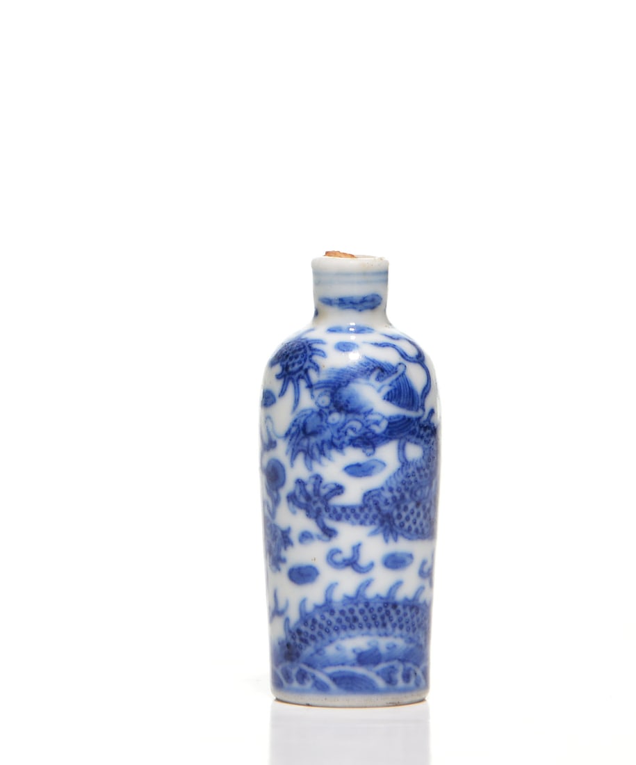 Chinese Blue And White Dragon Snuff Bottle: Bottle of slender ovoid form, delicately painted in rich shades of underglaze blue with a dynamic dragon pursuing a flaming pearl amidst an ethereal landscape of scrolling clouds. The serpentine body