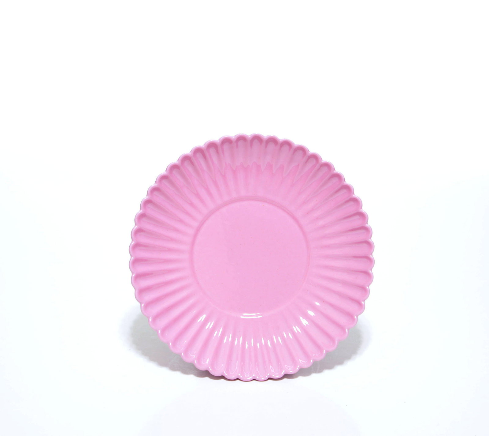 Chinese Pink-Enameled Dish: The shallow circular porcelain dish is molded with radiating flutes and a scalloped rim, rising from a short tapered foot. It is covered overall in a glossy pink glaze, the base left white and