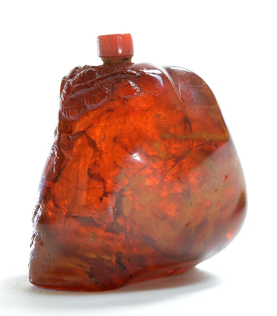 Chinese Amber Snuff Bottle: Of flattened pear form, the translucent reddish-orange body is carved in high relief with a sinuous dragon winding around the sides, its scaled body and head emerging at the shoulder. The material