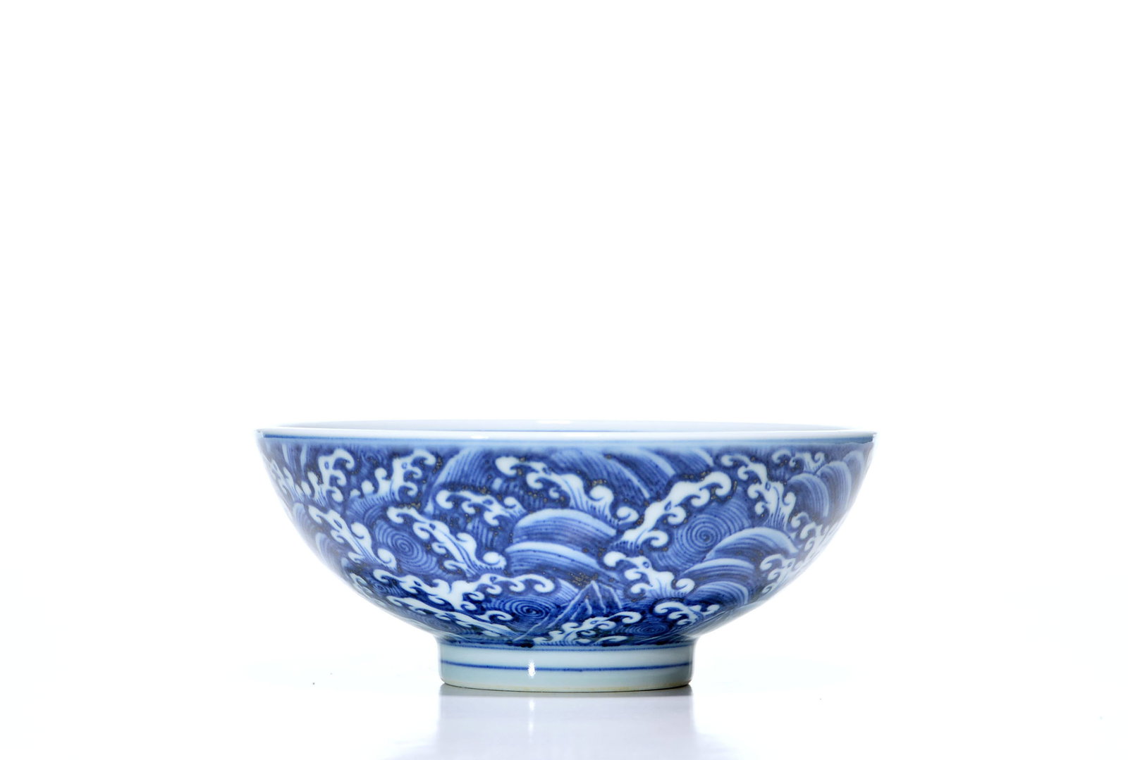 Chinese Blue and White 'Wave' Bowl: The rounded bowl is supported on a short, slightly flared foot and decorated in underglaze blue with a continuous design of cresting waves and whirlpools. The interior is painted with a circular wave