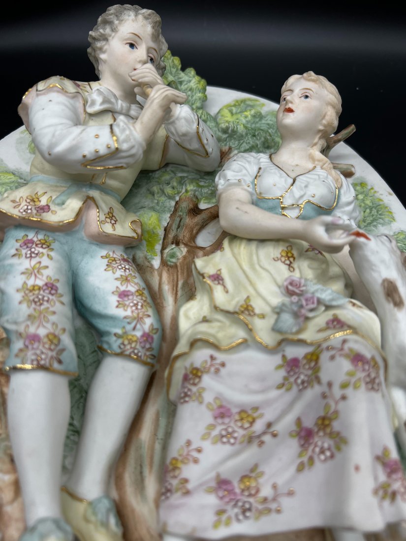 Sculpted Figures Of A Young Man And A Young Woman On A Hand Painted Plate: Sculpted Figures Of A Young Man And A Young Woman On A Hand Painted Plate. The young man appears to be playing the flute and the young woman is feeding a calf or goat. They are sitting in the forest s
