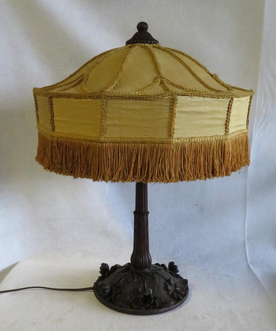 Black Forest styled carved wooden table lamp with leaf: Black Forest styled carved wooden table lamp with leaf base and carved and reeded finial. Handmade gold silk shade with woven string borders – early 20th century. Some losses to leaves on base, seve