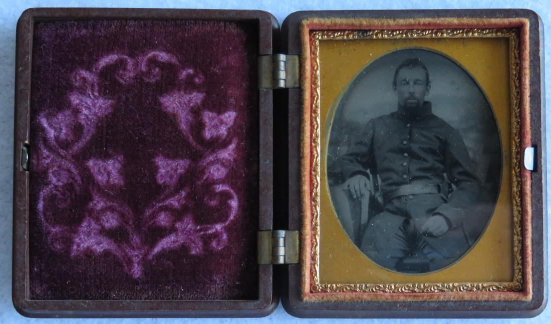 Tintype of Civil War soldier seated at table - an: Tintype of Civil War soldier seated at table - an American flag appears to be covering the table where his kepi is placed - 9th plate in gutta percha case with patriotic motif including flags and shie