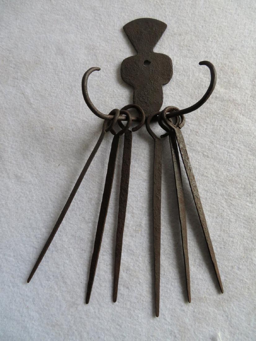 Hand forged iron skewer set with 6 skewers, mustache: Hand forged iron skewer set with 6 skewers, mustache shaped arms and shaped back-plate, late 18th to early 19th century - the skewers 8.5"H, total height 14.5". Very good original condition.