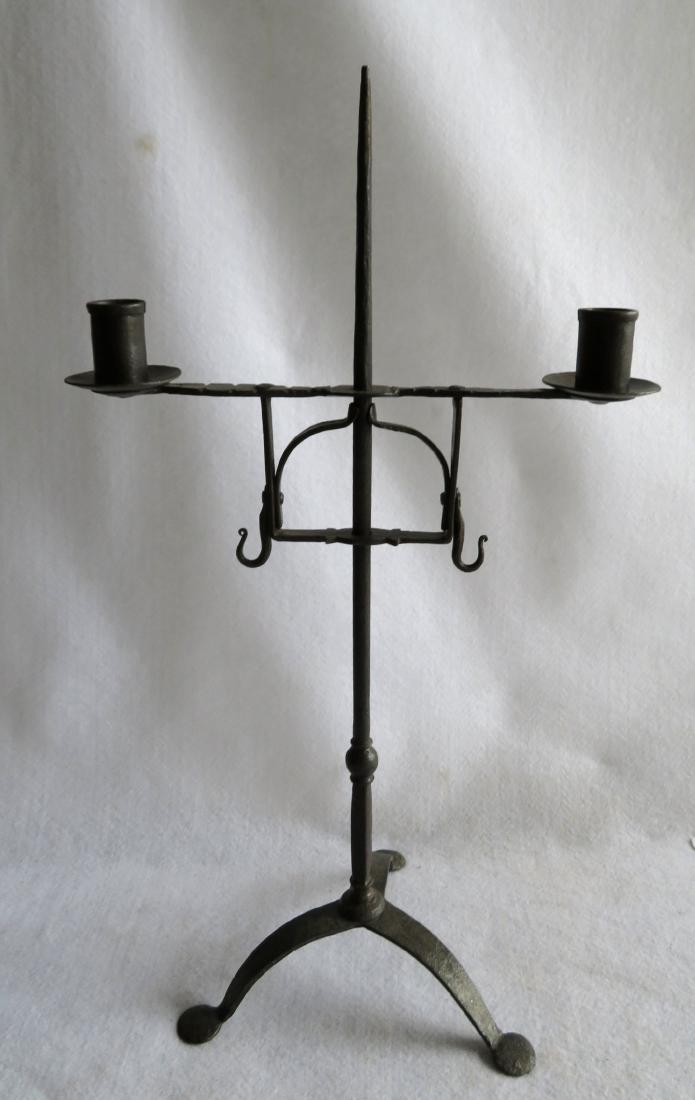 Early hand forged revolving iron lighting device having: Early hand forged revolving iron lighting device having a double candle fonts, the stand on tripod base with tri-penny feet, and spring load adjuster for height - 18th century. Original black paint on