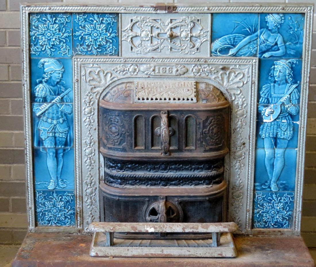 Cast iron stove that inserts into a fireplace with a: Cast iron stove that inserts into a fireplace with a front composed of ornate cast iron surrounded by blue tiles with figures of 3 musicians and various flowers - the tiles signed Trent and the stove'