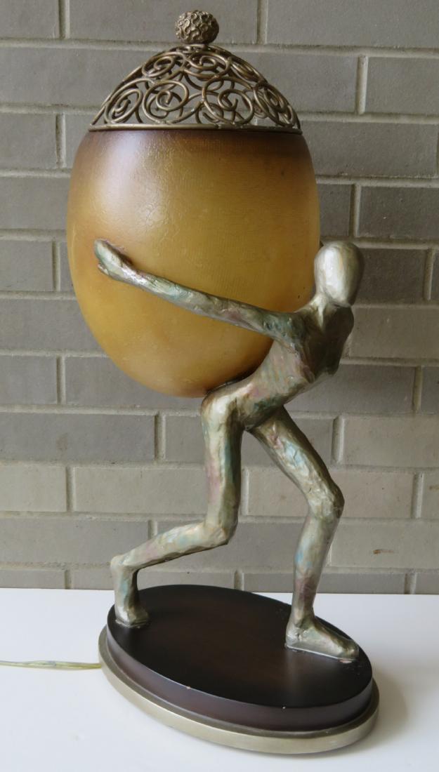 Mid-century figural table lamp/sculpture, depicting a: Mid-century figural table lamp/sculpture, depicting a stylized walking human figure carrying an egg shaped basket (the shade) on it's back with a removable and open work scrolled metal dome top with f