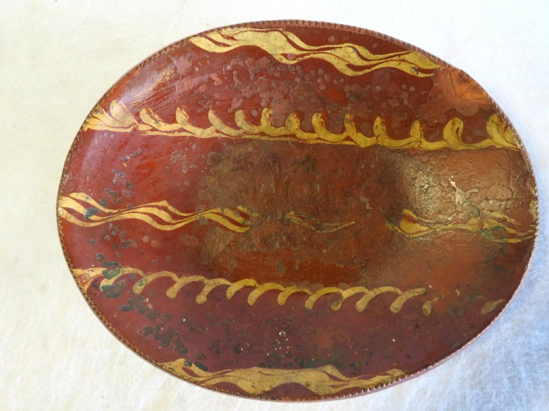 Redware platter decorated with slip wavy lines and also: Redware platter decorated with slip wavy lines and also have a coggled border, early 19th century. The surface with some losses to slip, a small repair along edge, the base with surface flaking in sev