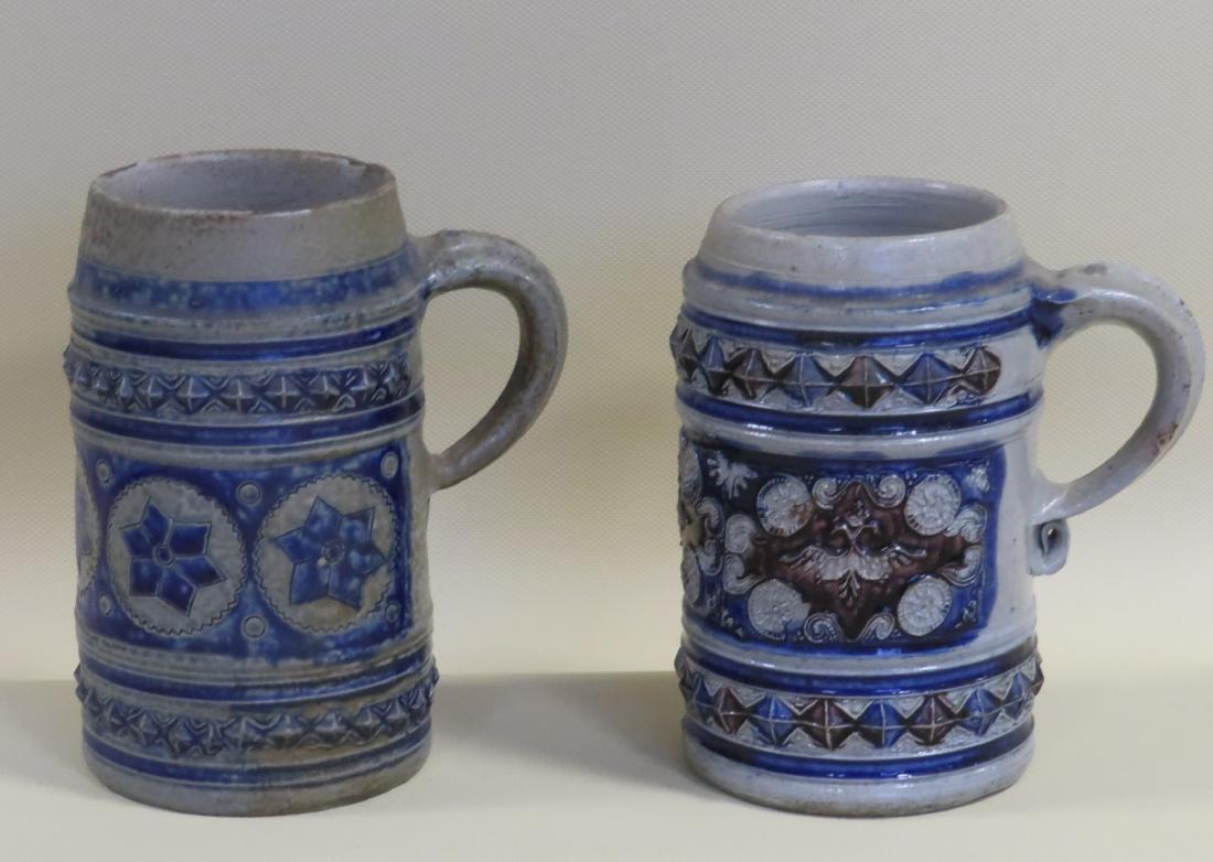 Two Westerwald mugs, each decorated with a row of: Two Westerwald mugs, each decorated with a row of diamonds above and below a central medallion, one with stars the other with scrolls and circular sundials - 5 3/4"H and 6"H. The smaller with a small