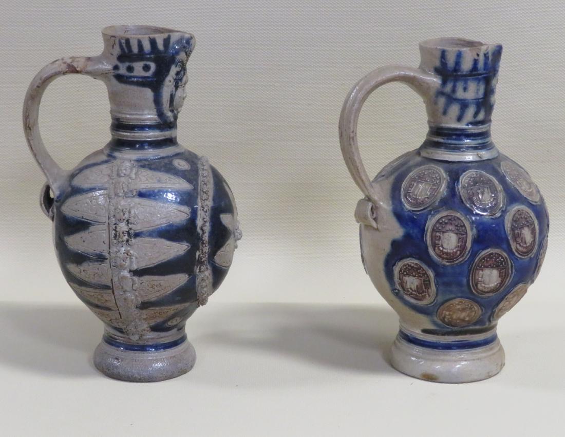 Two Westerwald jugs including: 1) Spout with face mask,: Two Westerwald jugs including: 1) Spout with face mask, the body decorated with 2 narrow vertical band of lions' heads down the sides and the front decorated with a large incised flower within a medal