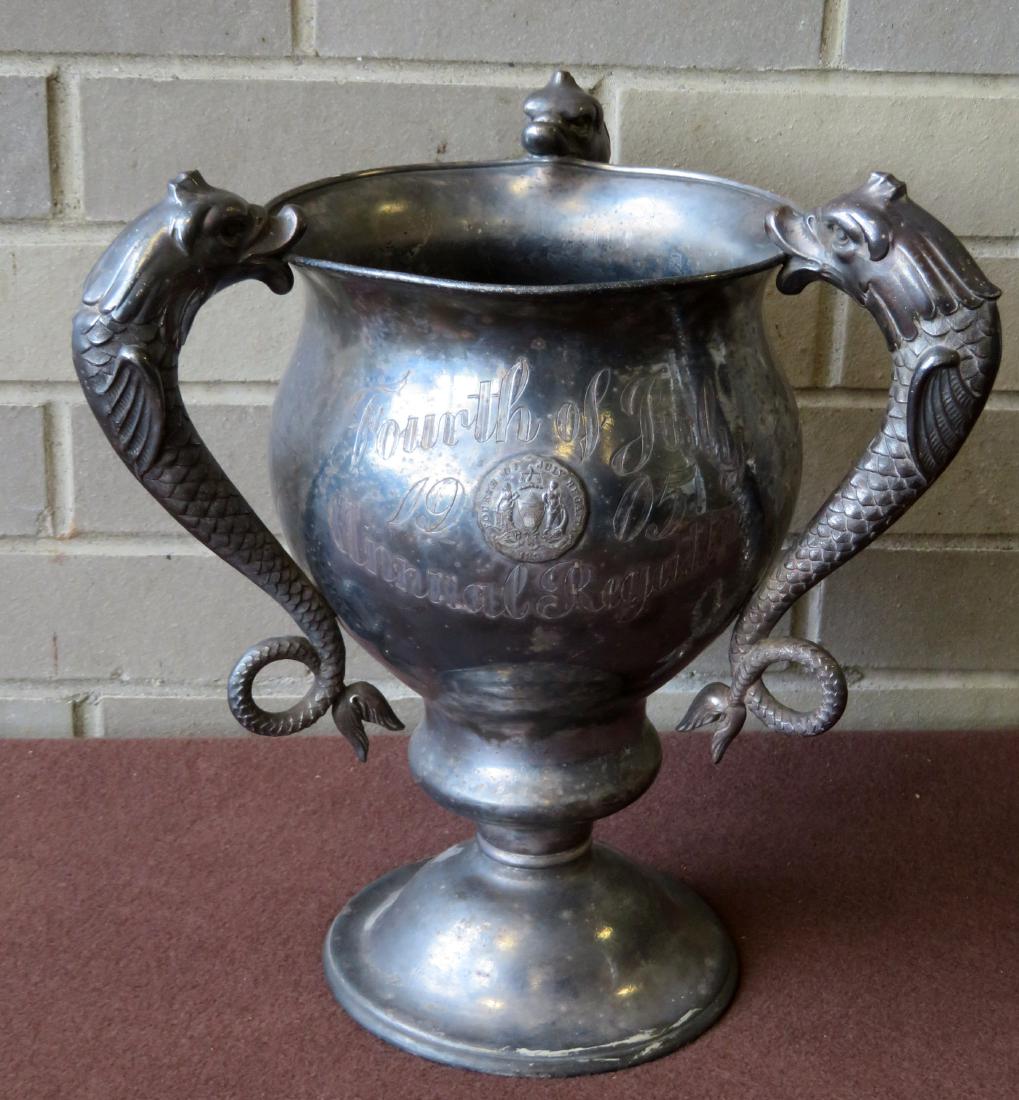A silver boating trophy cup with 3 dolphin shaped: A silver boating trophy cup with 3 dolphin shaped handles, inscribed across the front "Fourth of July 1905 / Annual Regatta". Losses to silver plate, otherwise good condition. Signed on base "J.E. Cal