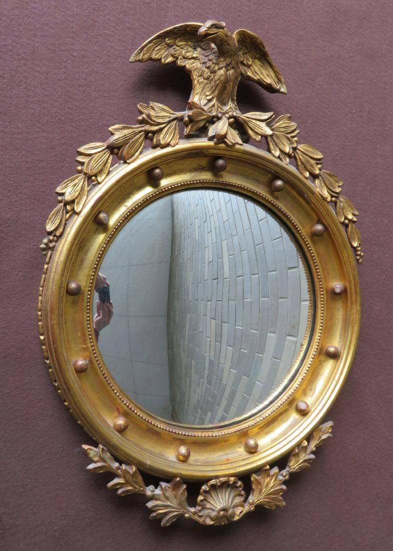 Federal style convex gilded bullseye wall mirror having: Federal style convex gilded bullseye wall mirror having a crest with a carved wooden spread wing eagle pediment over wreath and having a matching wreath with seashell across the base. The mirror with 