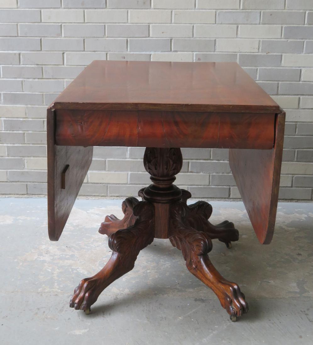 Empire mahogany drop-leaf breakfast table with a: Empire mahogany drop-leaf breakfast table with a heavily carved base having an acanthus center pedestal leading to acanthus knees and lion's paw feet. Some swelling to the mahogany veneer apron on bot
