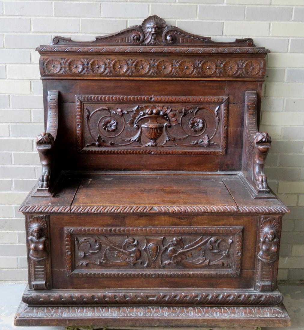 Heavily carved Victorian hall seat having a lion's face: Heavily carved Victorian hall seat having a lion's face and scrolled crest with other carvings over a profusely carved seat back decorated with a central panel of scrolls an urn of fruit and flowers. 