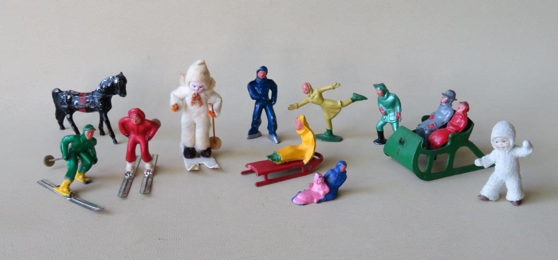 Grouping of miniature hand painted figures performing: Grouping of miniature hand painted figures performing winter sports including: Two lead skiers (one with losses to 1 ski), 2 lead skaters, lead boy on sled, lead seated mother and baby (missing sled),