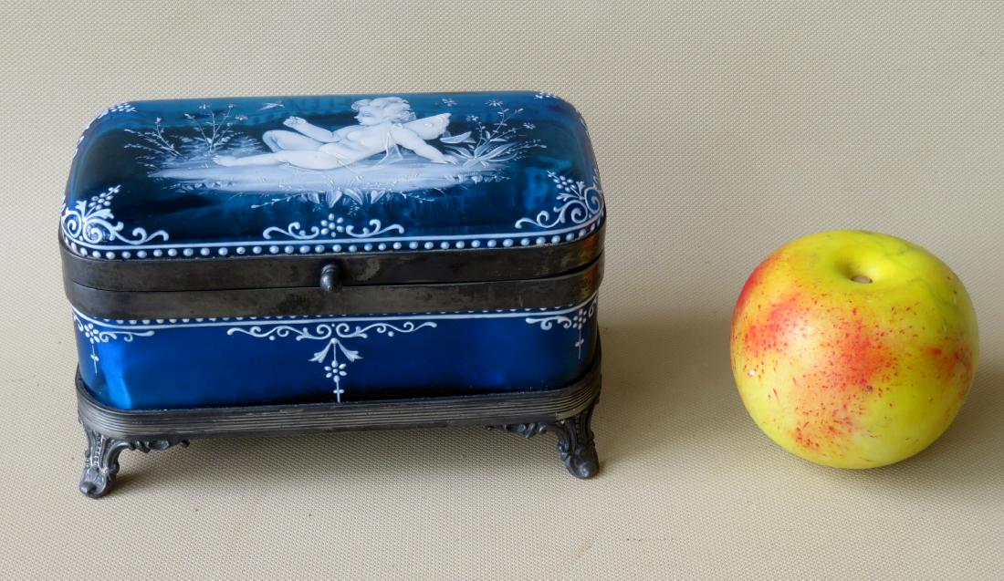 A beautiful Mary Gregory blue glass covered dresser box: A beautiful Mary Gregory blue glass covered dresser box on silver plate frame with scrolled feet. White enameling including the lid decorated with a cherub, bird, butterfly and flowers. 19th century. 