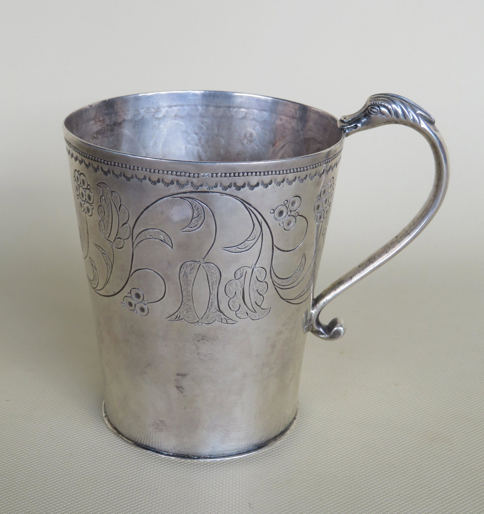 Early silver cup with sea serpent handle and having: Early silver cup with sea serpent handle and having etched flowers on a vine, including tulips, around the perimeter - the engraved initials under the flowers marked "P B S", probably 18th century. No