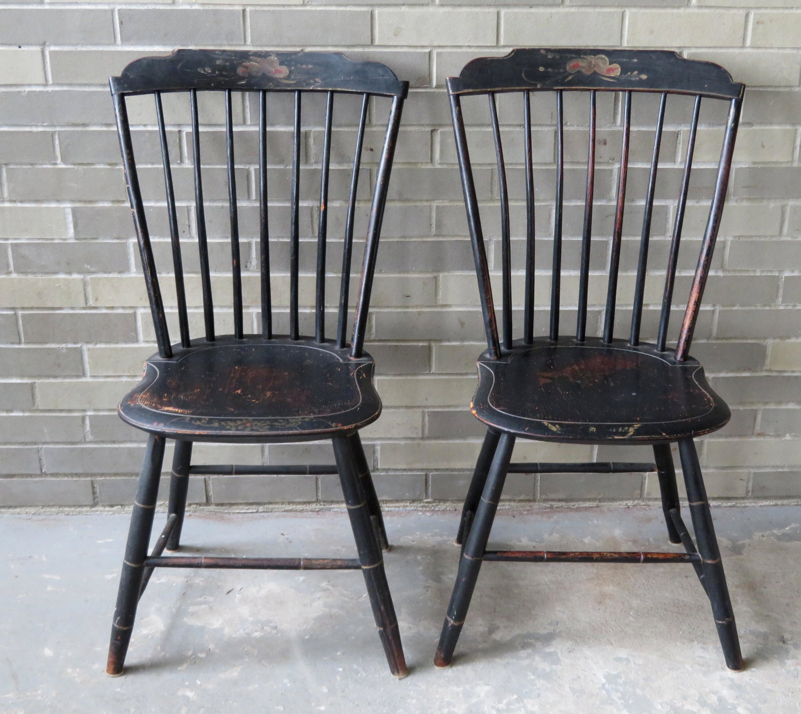 Pair of step-down Windsor side chairs in old black: Pair of step-down Windsor side chairs in old black paint with hand painted floral painting across the top rail and across the front of the saddle seat, signed D.G.B. in white on reverse of seat. Both 