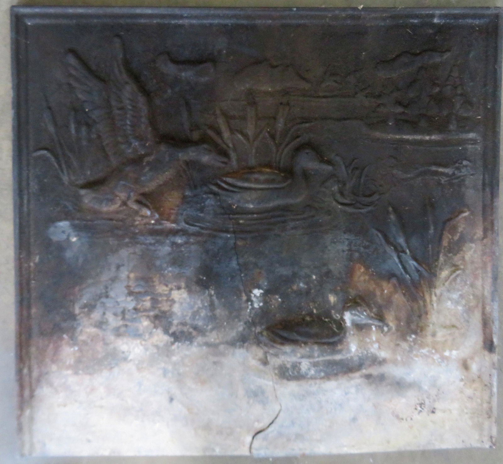 Cast iron fireback decorated with embossed ducks in: Cast iron fireback decorated with embossed ducks in marshland, 22" x 24". A 13" hairline extends upward from the center of the base. 20th century.