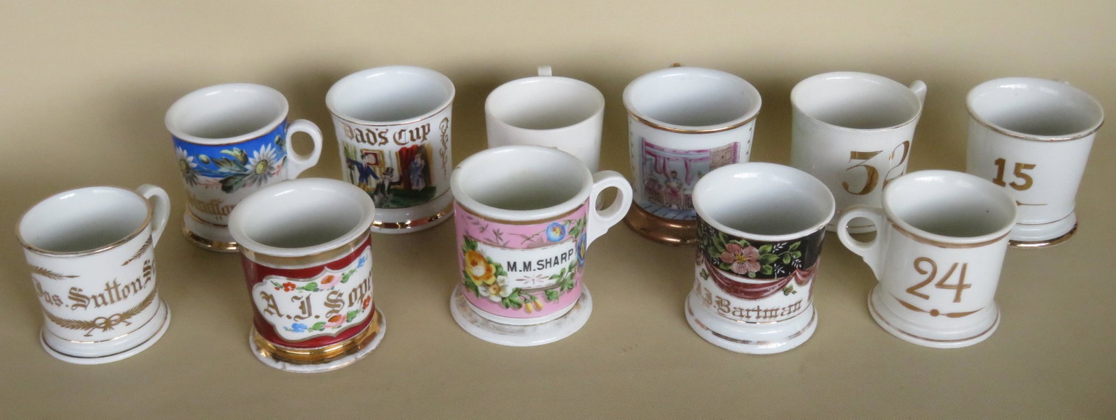 A grouping of 11 shaving mugs, most hand painted and: A grouping of 11 shaving mugs, most hand painted and several with the names of owners. Others with a gold barber shop number on the front side. One occupational hand colored transferware of the interi