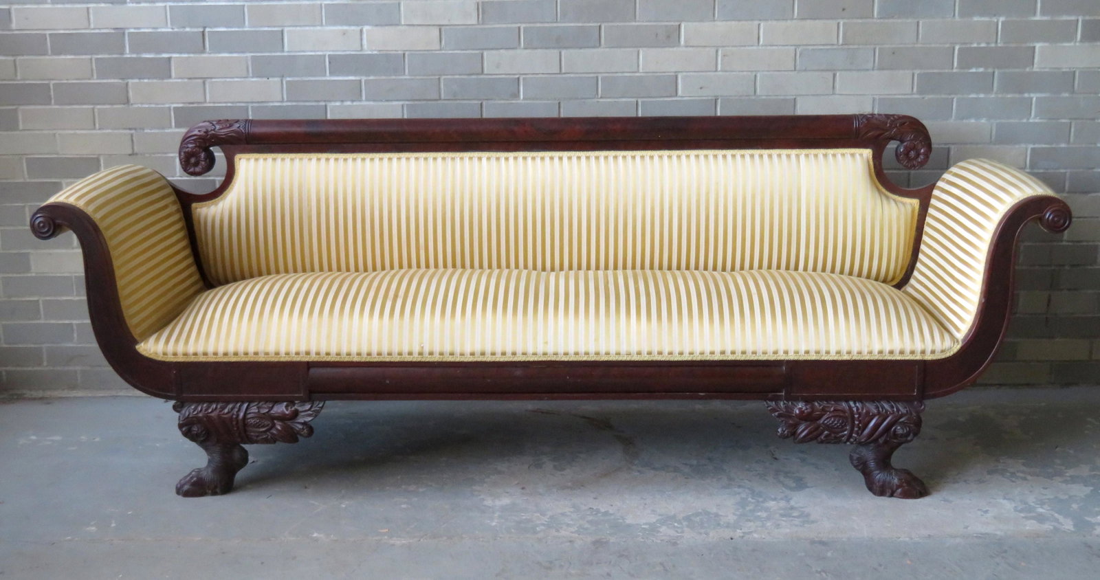 A classical federal upholstered sofa with a carved: A classical federal upholstered sofa with a carved mahogany frame that includes a rolled crest with acanthus decoration and rosette terminals, scrolled arms, and a carved horn of plenty attached to ha
