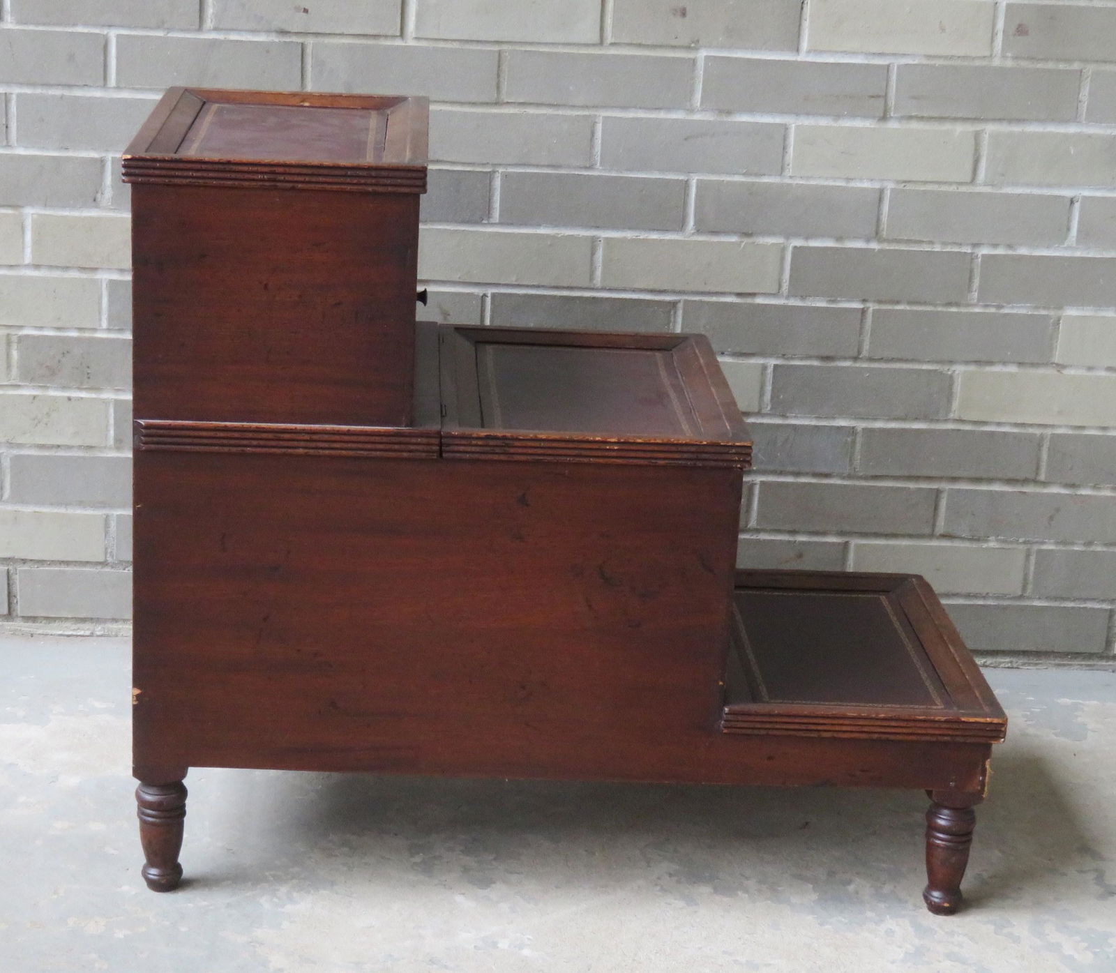 A Sheraton style mahogany bedstep having 3 steps with: A Sheraton style mahogany bedstep having 3 steps with tooled leather tops (probably replacement leather). The top step with a built-in cupboard, and the second step with lift-top storage compartment.