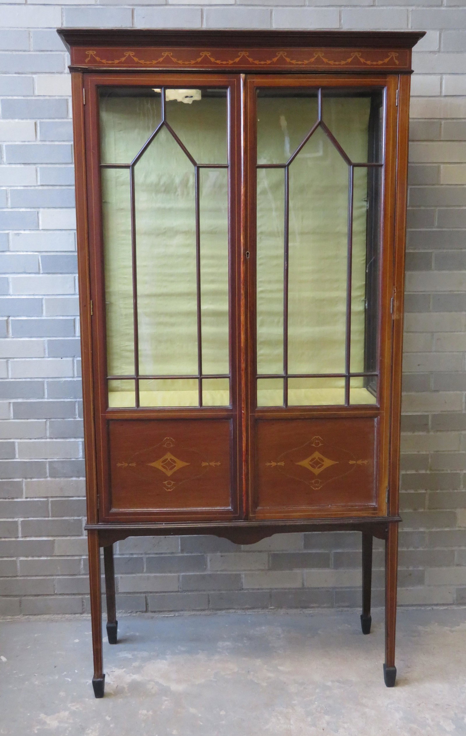 An Edwardian mahogany lighted showcase with glass: An Edwardian mahogany lighted showcase with glass panels on all sides. The crest with bell flowers on ribbon inlays - the doors with line inlay and each with 8 lights (real mullions between glass) ove