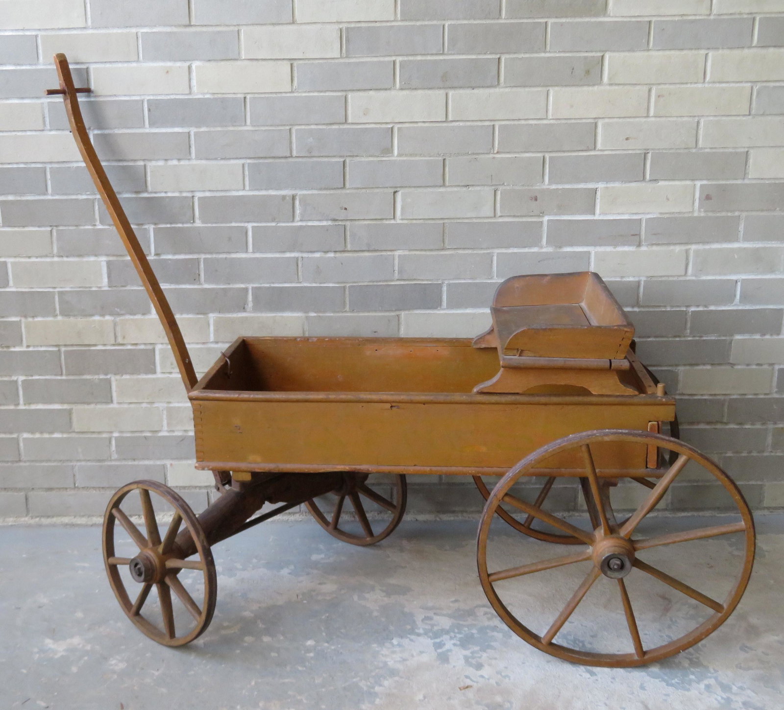 Child's pull wagon with wooden wheels and original: Child's pull wagon with wooden wheels and original removable buggy seat in old mustard paint. Very good condition. 32"L x 16 1/2"W(box) x 18 1/2" to top of seat x handle 36 3/4"L. Circa 1880.