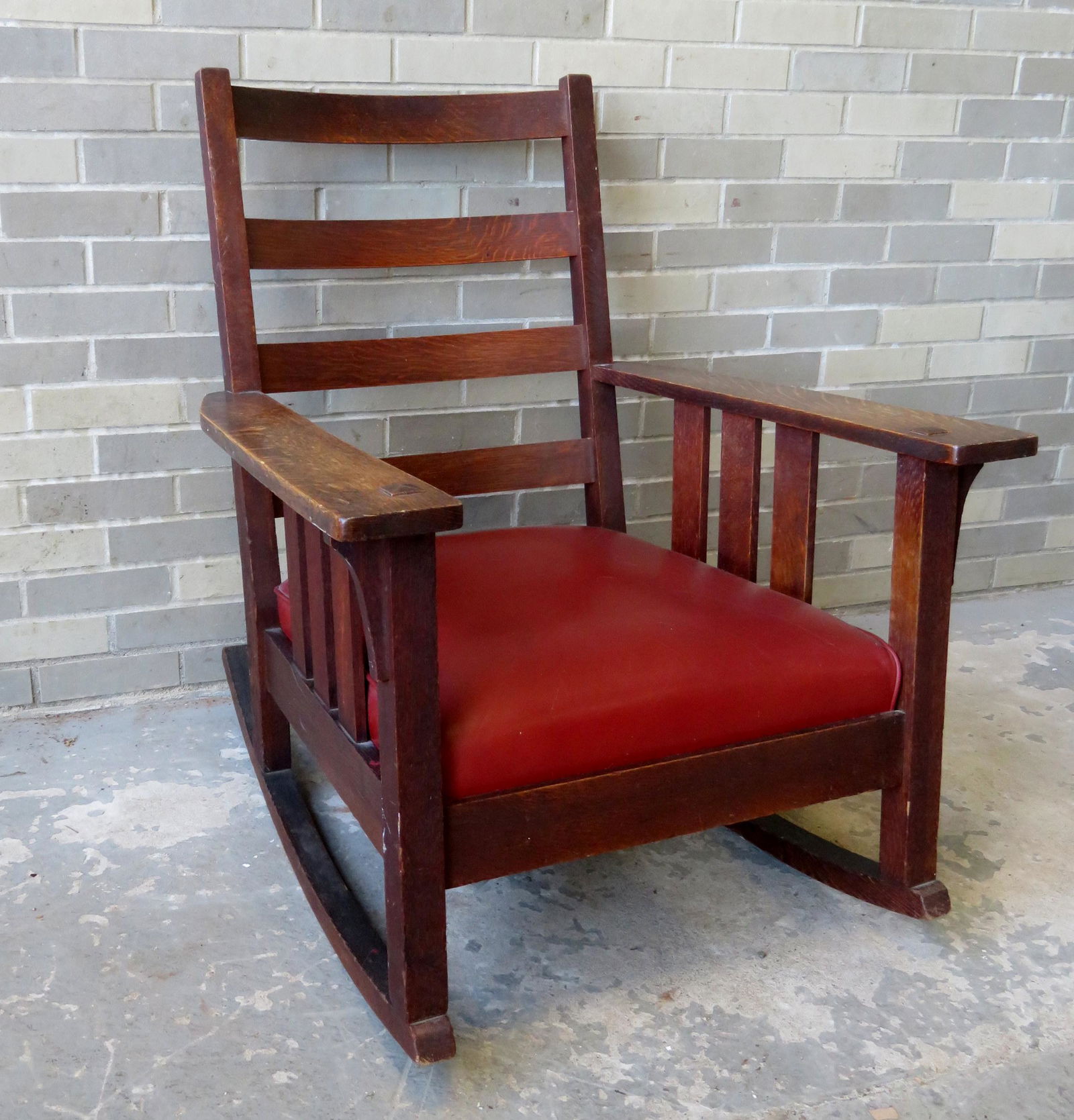 Mission oak rocker having 4 curved horizontal slats: Mission oak rocker having 4 curved horizontal slats across the back and 3 vertical slats under each arm, original finish. Newer leather upholstery with some surface scratches. Overall very good condit