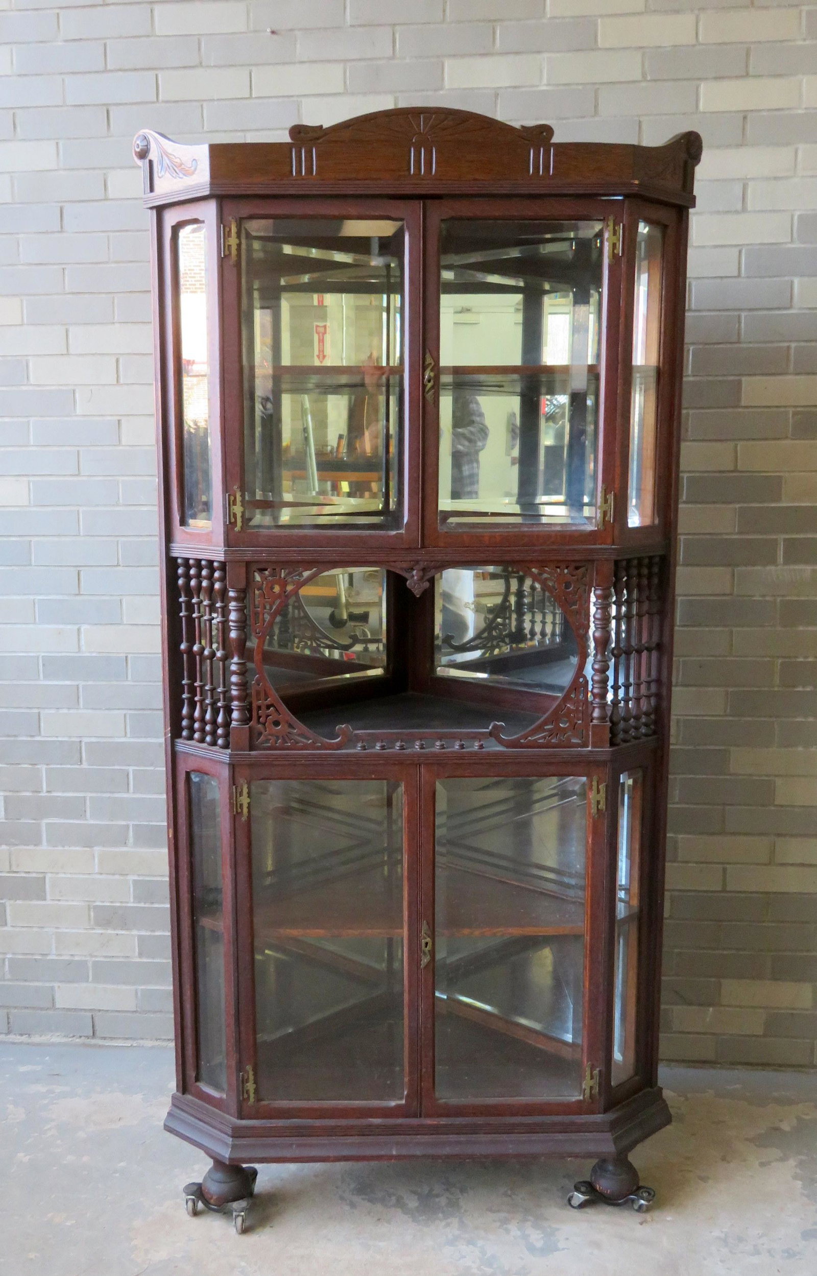 R.J. Horner oak corner cabinet having a carved cornice: R.J. Horner oak corner cabinet having a carved cornice over 2 beveled glass doors, over an open shelf with stick & ball & filigree decorations, over 2 beveled glass doors resting on ball feet. The sid