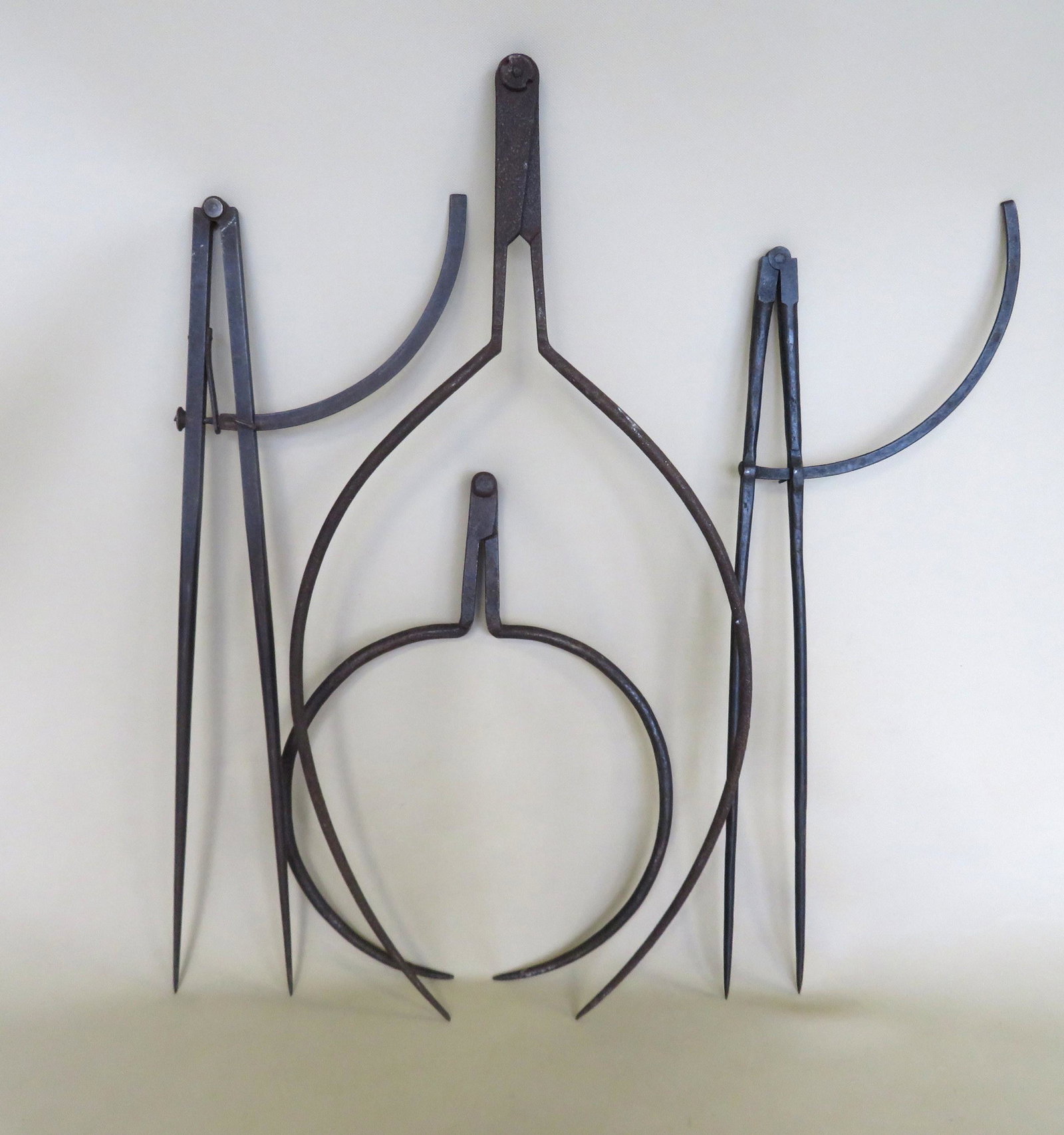 Four early iron measuring devices including 2 hand: Four early iron measuring devices including 2 hand forged calipers, the largest 28"L x 11 1/2", both in very good condition; and 2 compasses one hand forged, and one stamped R & E Mfg. Co. - the large