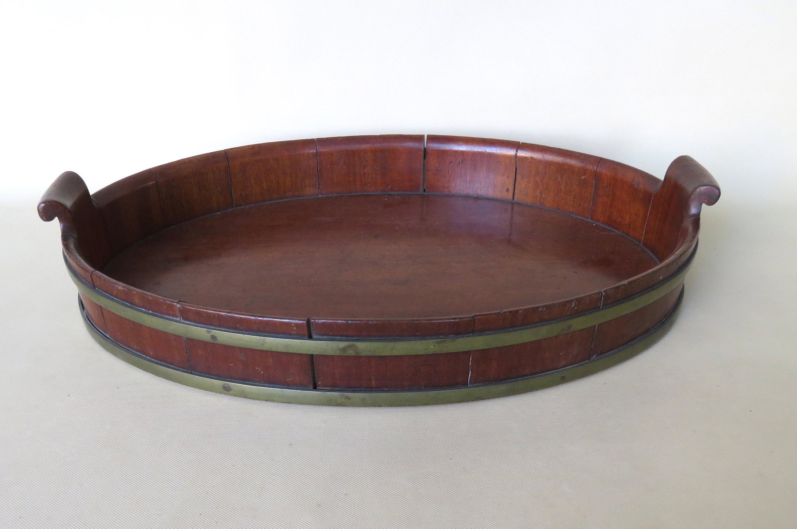 A Georgian mahogany brass bound tray with scrolled: A Georgian mahogany brass bound tray with scrolled handles on each end, early 19th century. The chamfered base is covered with felt, some of which is worn. Very good condition. 22 3/4"L x 15"W x 4"H.