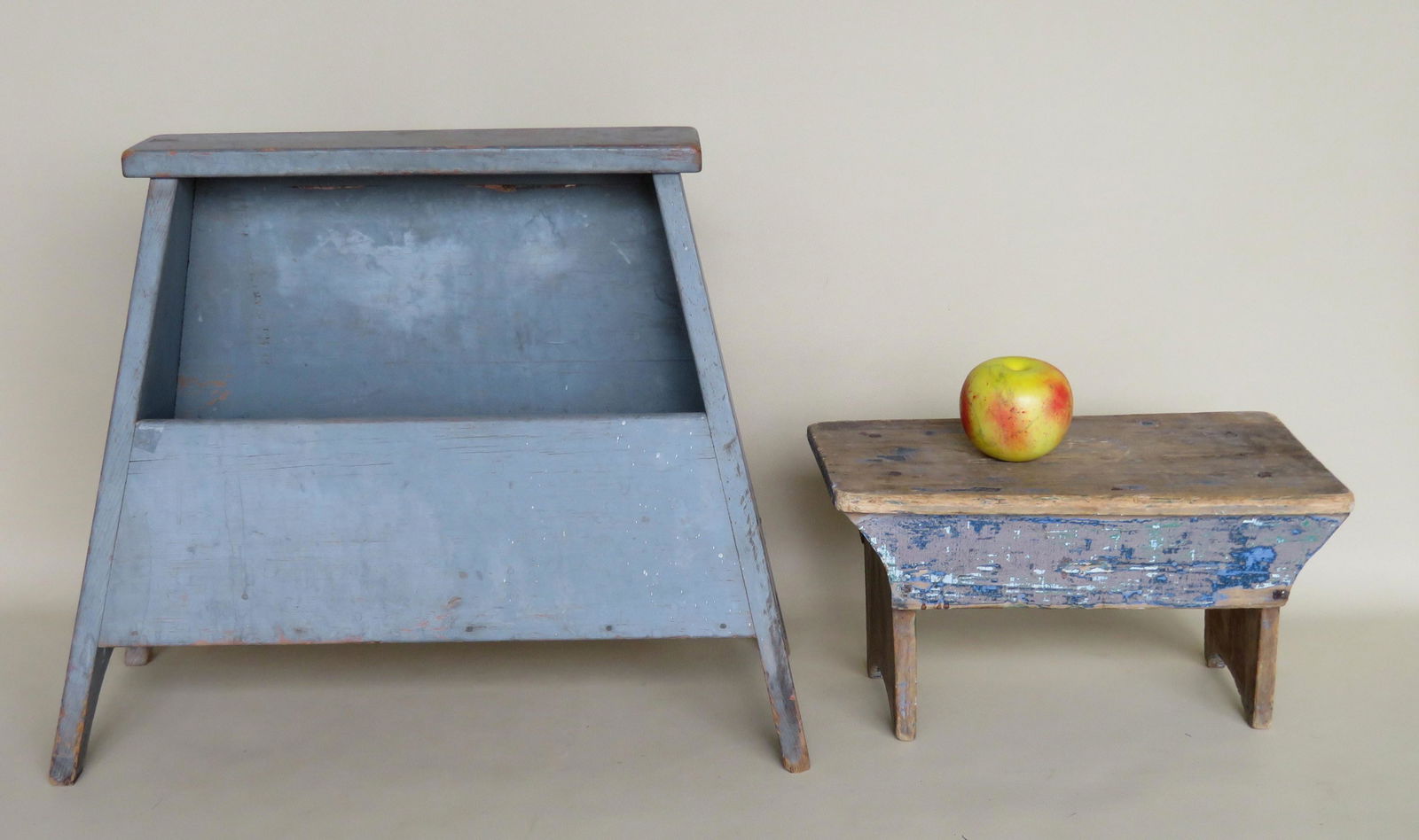 Two primitive cricket stools in old paint. The first: Two primitive cricket stools in old paint. The first with canted sides having 1/2 moon cutouts and a storage compartment in original blue/gray paint, 10 1/2"W x 9"D x 17H - early 20th century; the sec