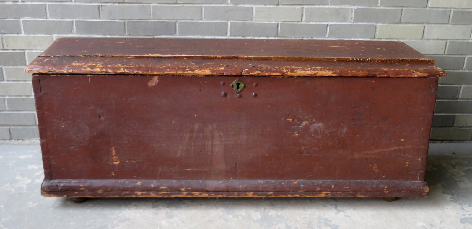 An early sea chest in original red paint having rattail: An early sea chest in original red paint having rattail hinges, molded edge to lid, interior till, original hand forged lock, small turned feet, and canted sides. Dovetailed and rosehead nail construc