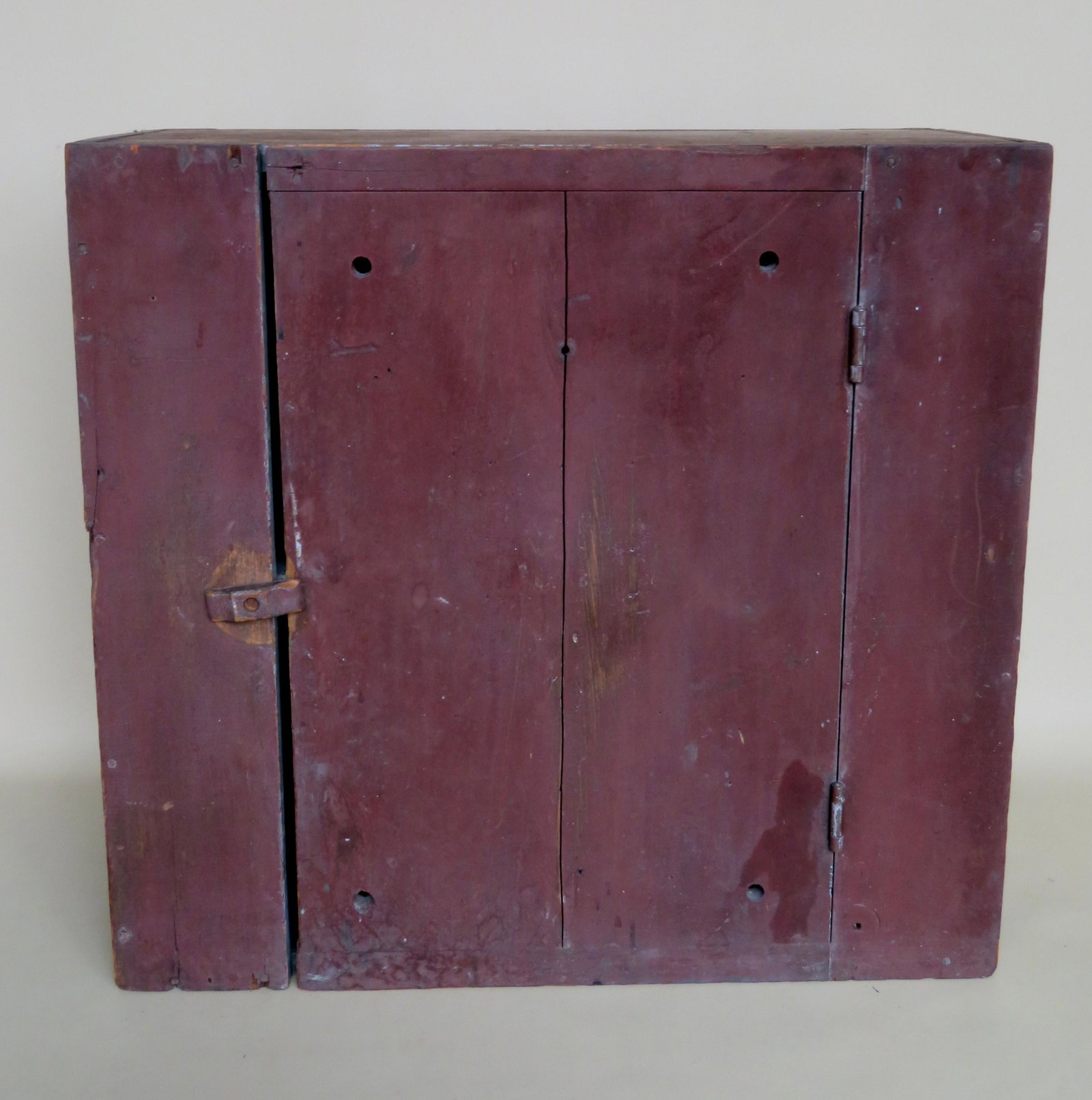 A primitive wall mounted pie safe having 1 single door: A primitive wall mounted pie safe having 1 single door in original red paint, late 19th century. Small air holes are drilled into the front door and side panels to provide circulation. Some use wear b