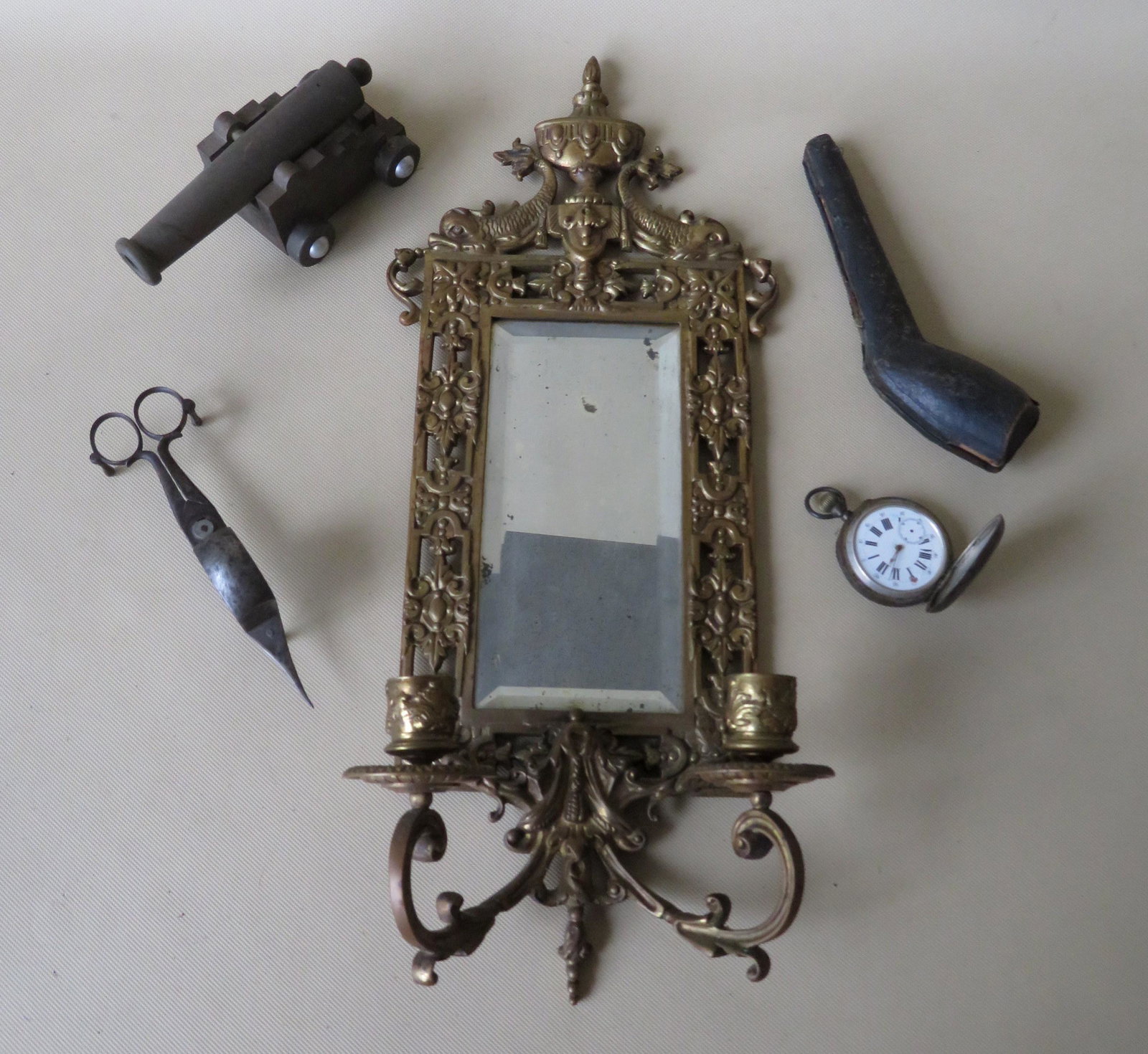 A grouping of 5 decorative objects including: An ornate: A grouping of 5 decorative objects including: An ornate brass wall mirror and double wall sconce - the mirror with beveled glass, and the crest decorated with 2 dolphins flanking a flaming urn - late 