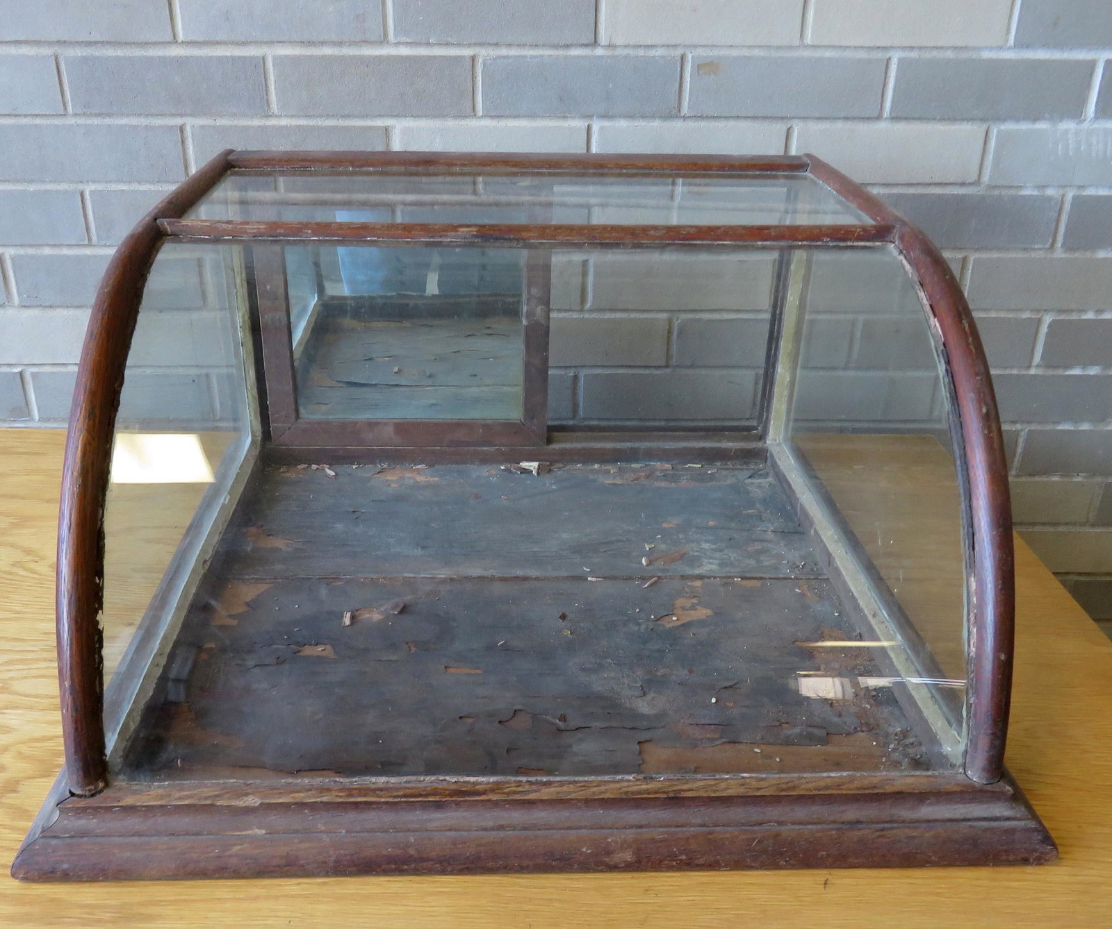 Small table top oak showcase with curved front and oak: Small table top oak showcase with curved front and oak frame, having 2 sliding glass doors with mirror backs. 23 1/2"W x 23"D x 12"H. Condition: Original finish, oak frame slightly loose from glass (n