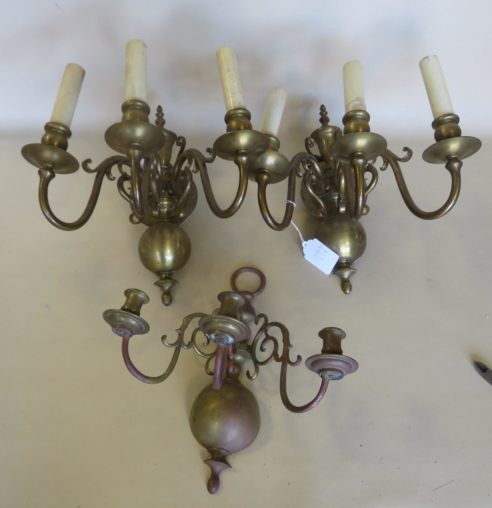 Three brass wall sconces, each with 3 lights: Two: Three brass wall sconces, each with 3 lights: Two matching that are electrified and possibly were gas originally; the third is a candle sconce. All circa 1900. Each approximately 16"H x 14"W x 11"D. A