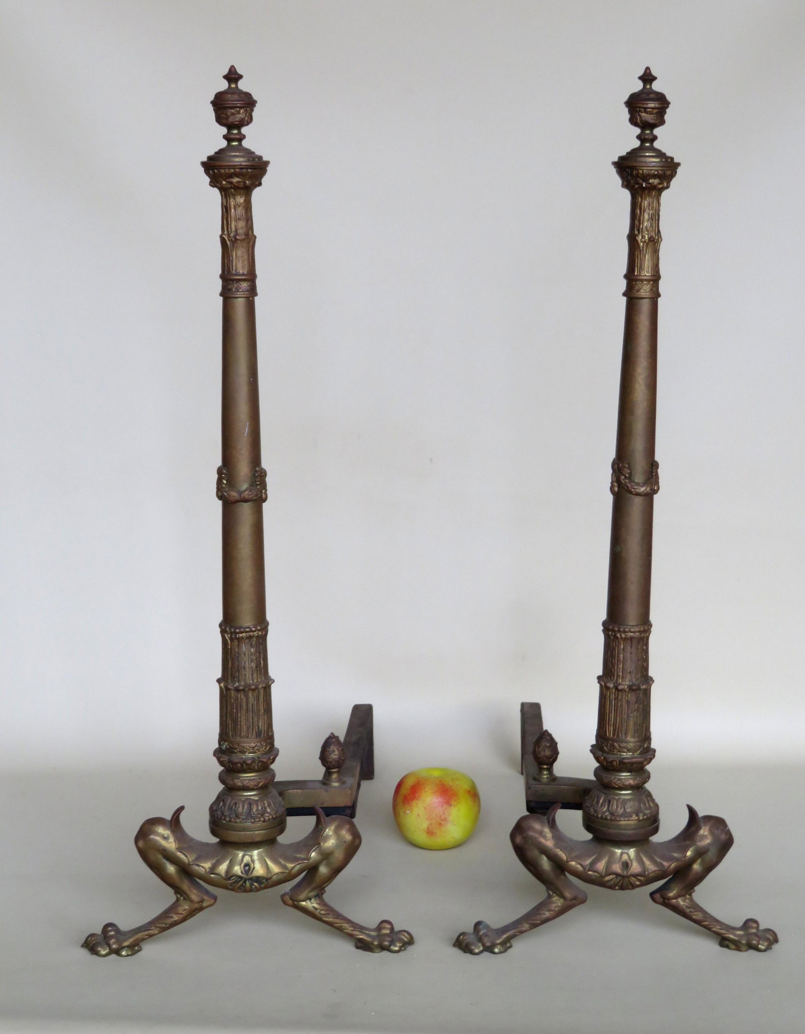 Pair of ornate French brass andirons with urn finials: Pair of ornate French brass andirons with urn finials over taper column leading to dragon legs with claw feet. 26 1/2"H x 21"D. Probably early 20th century.