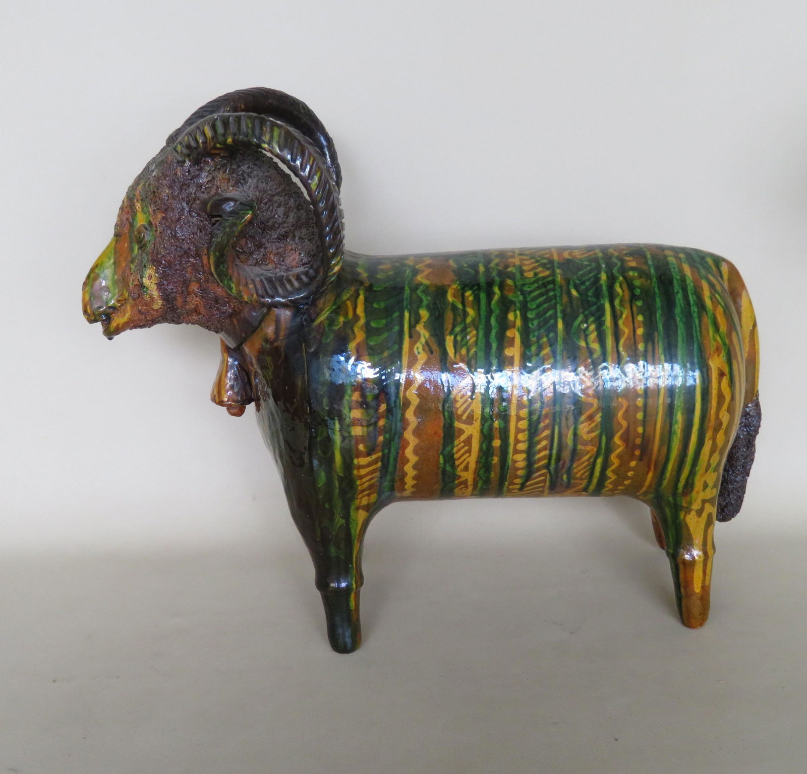 A large unusual redware standing ram wearing bell, with: A large unusual redware standing ram wearing bell, with brown, green and yellow slip decorations, incised initials and date on belly - 1979. Loss on end of one horn where it wraps to meet his right ea