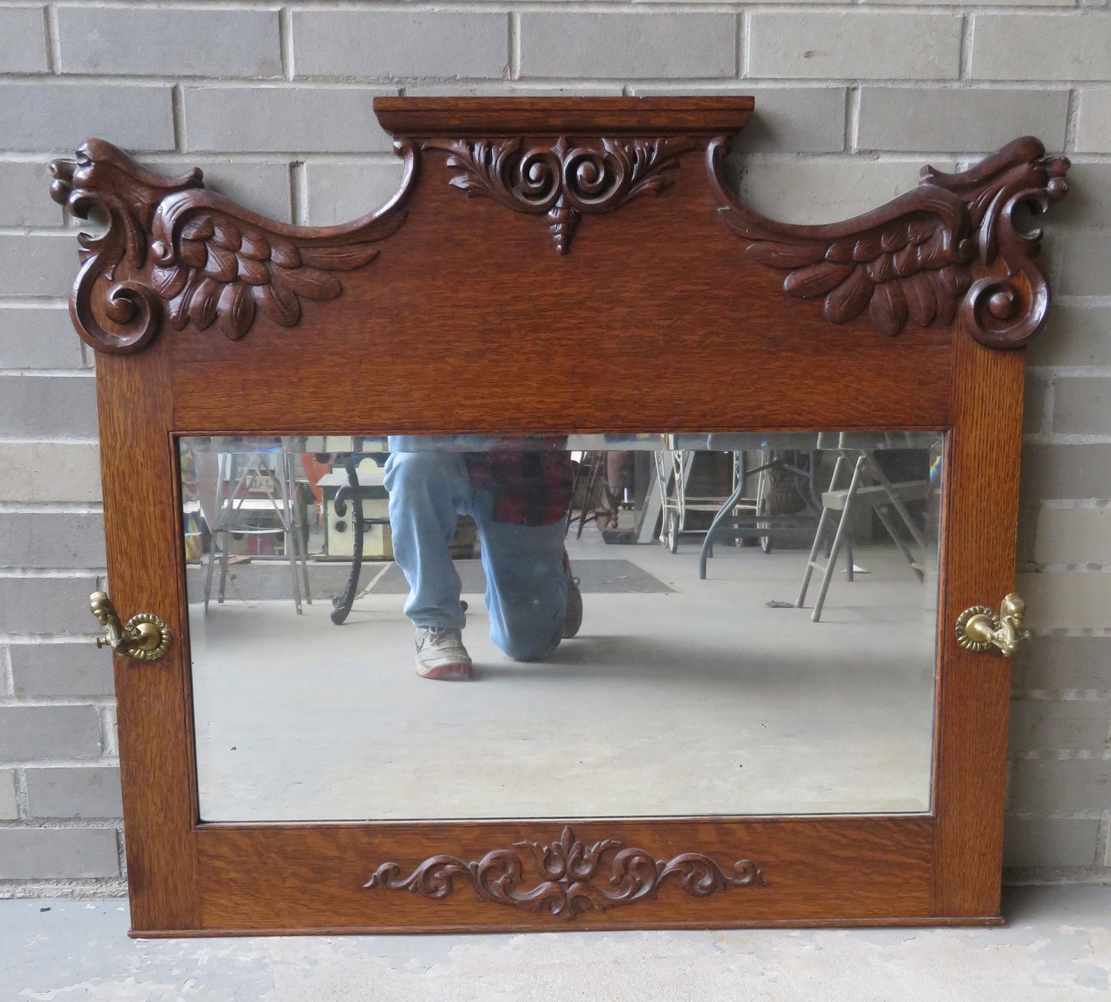 Oak wall mirror having griffin faces on top of ends and: Oak wall mirror having griffin faces on top of ends and having 2 brass griffin form hat hooks. Late 19th century. 37 1/4"W x 32 1/2"H. Very good condition.