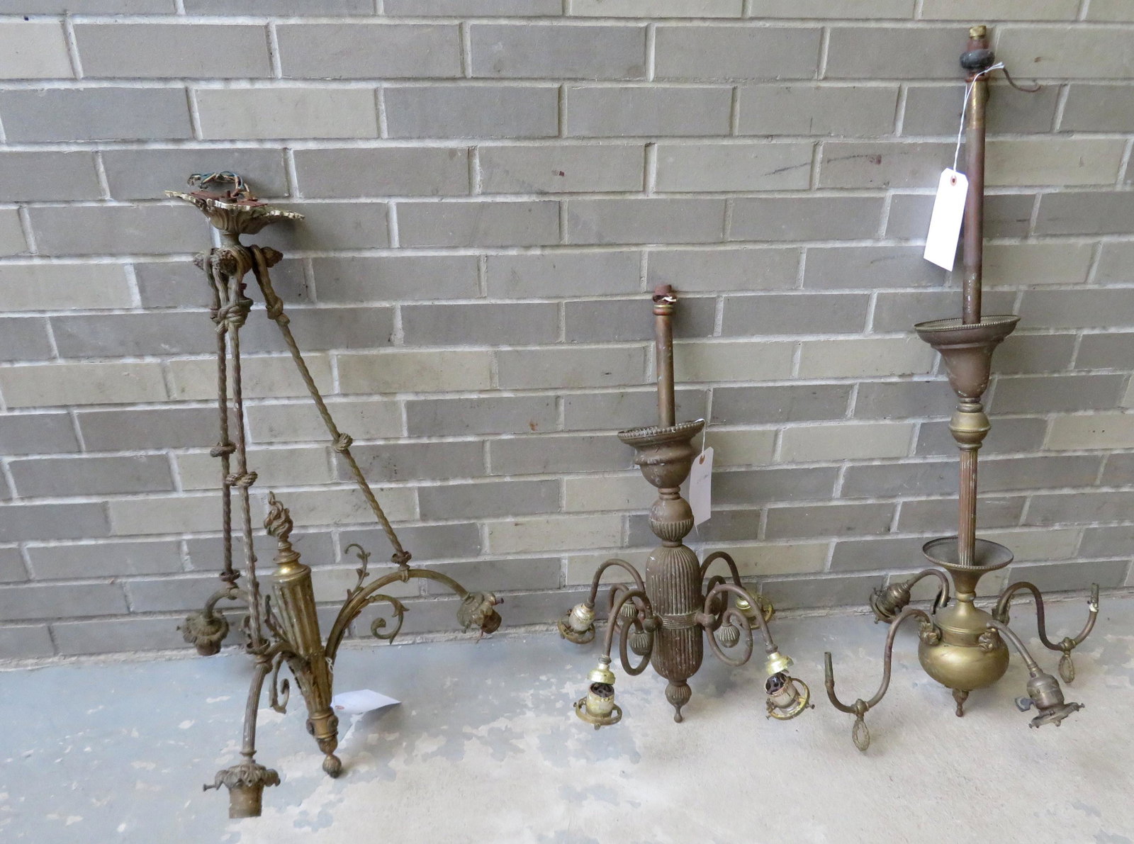 Three fancy brass chandeliers including: 1) Has 3 brass: Three fancy brass Victorian chandeliers including: 1) Electric with 3 brass ropes that lead from the ceiling cover to the 3 lighting arms and having a central fluted post with flame finial - 39"H x 20