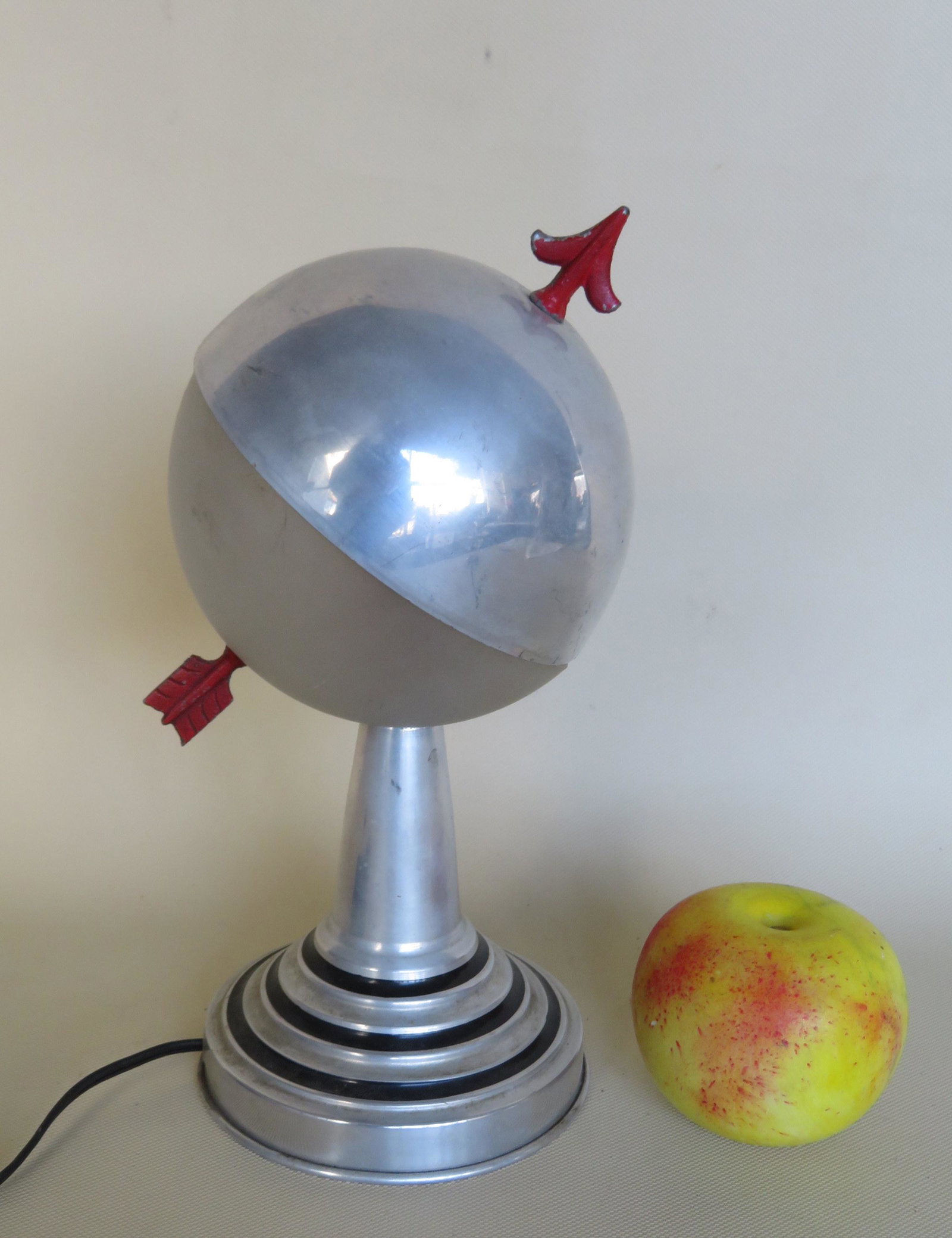 Small mid-century aluminum table lamp in the form of an: Small mid-century aluminum table lamp in the form of an armillary - the arrow in original red paint and the stepped concentric base with original black paint highlights - note that 1/2 the sphere is a