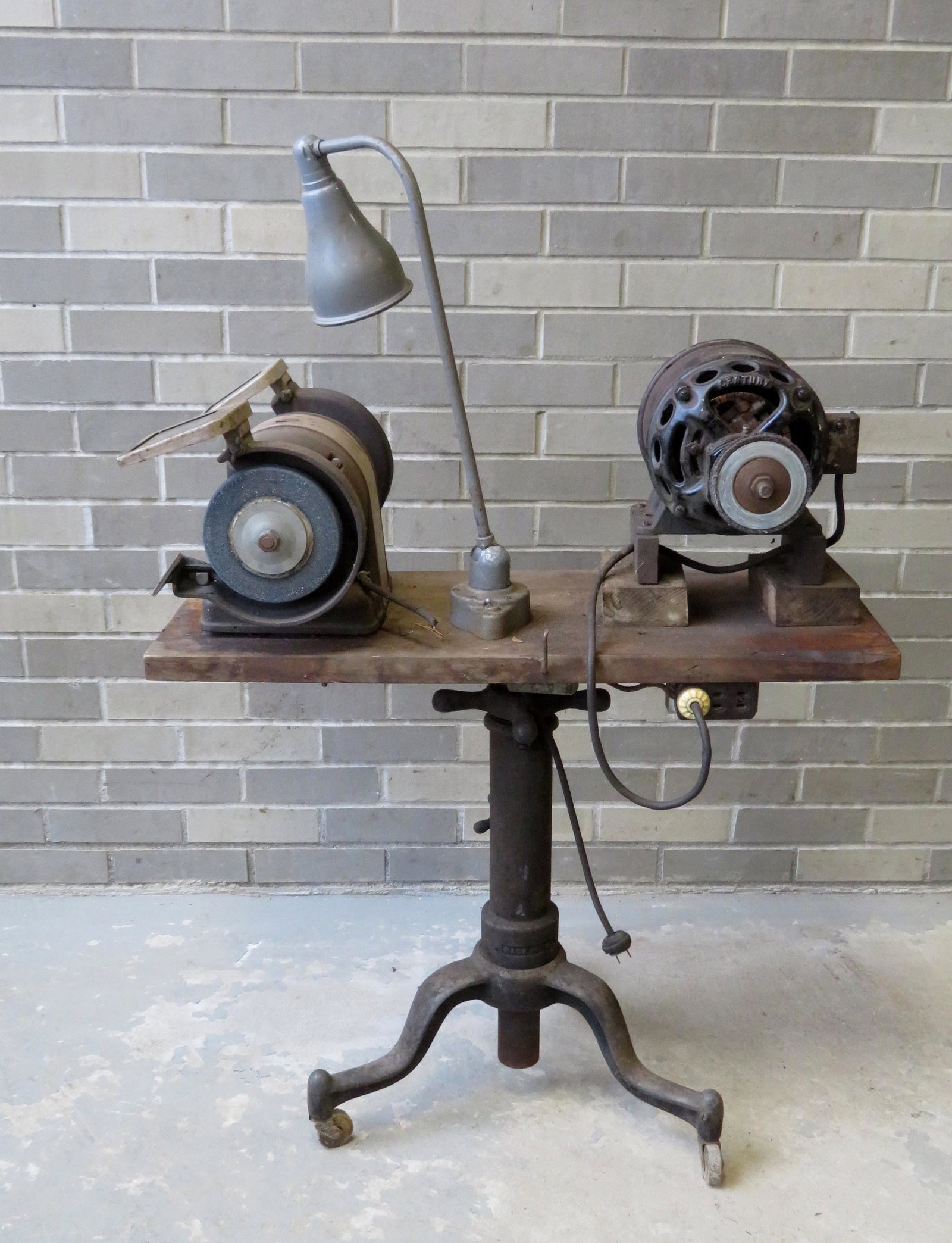 Architects table circa 1900 and grinding wheels.: An architects adjustable table with adjustable wooden top attached to adjustable iron base on wheels. The top converted to a work table with a vintage Century Single Phase Motor (polisher)with patent 