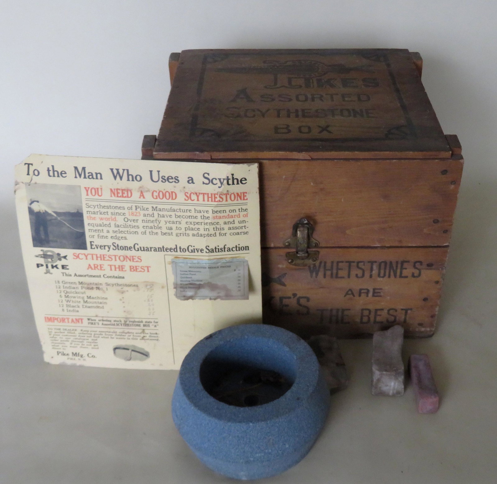 Advertising box for Pike's Scythe stones.: Wooden advertising box and cardboard advertisement for Pike's scythestones, Pike Mfg. Co., Pike N.H.. The lid of the box with impressed marks of "PIkes Assorted Scythestone Box" - the logo of th compa