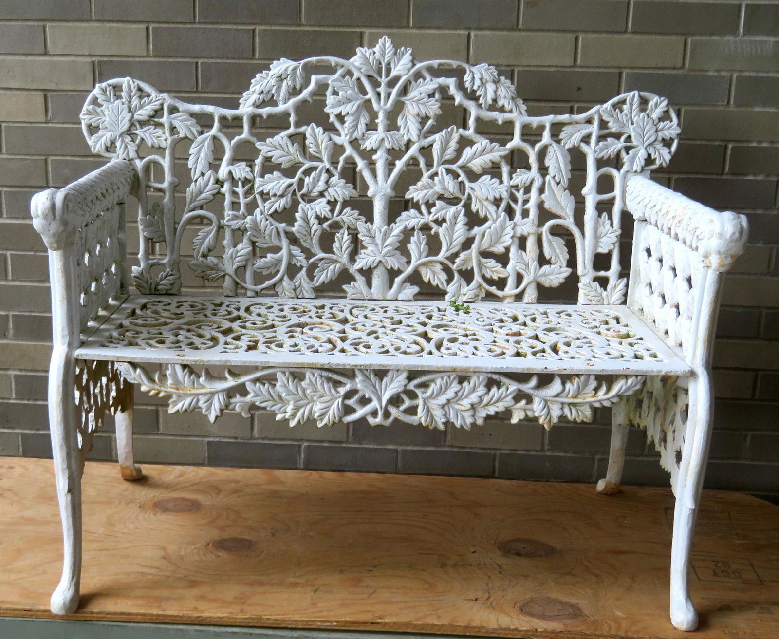A rustic cast iron garden bench, the back decorated: A rustic cast iron garden bench, the back decorated with branches and leaves, the seat with a pierced scroll-work design, the arms covered with leaves leading to ram's head terminals, the sides decora