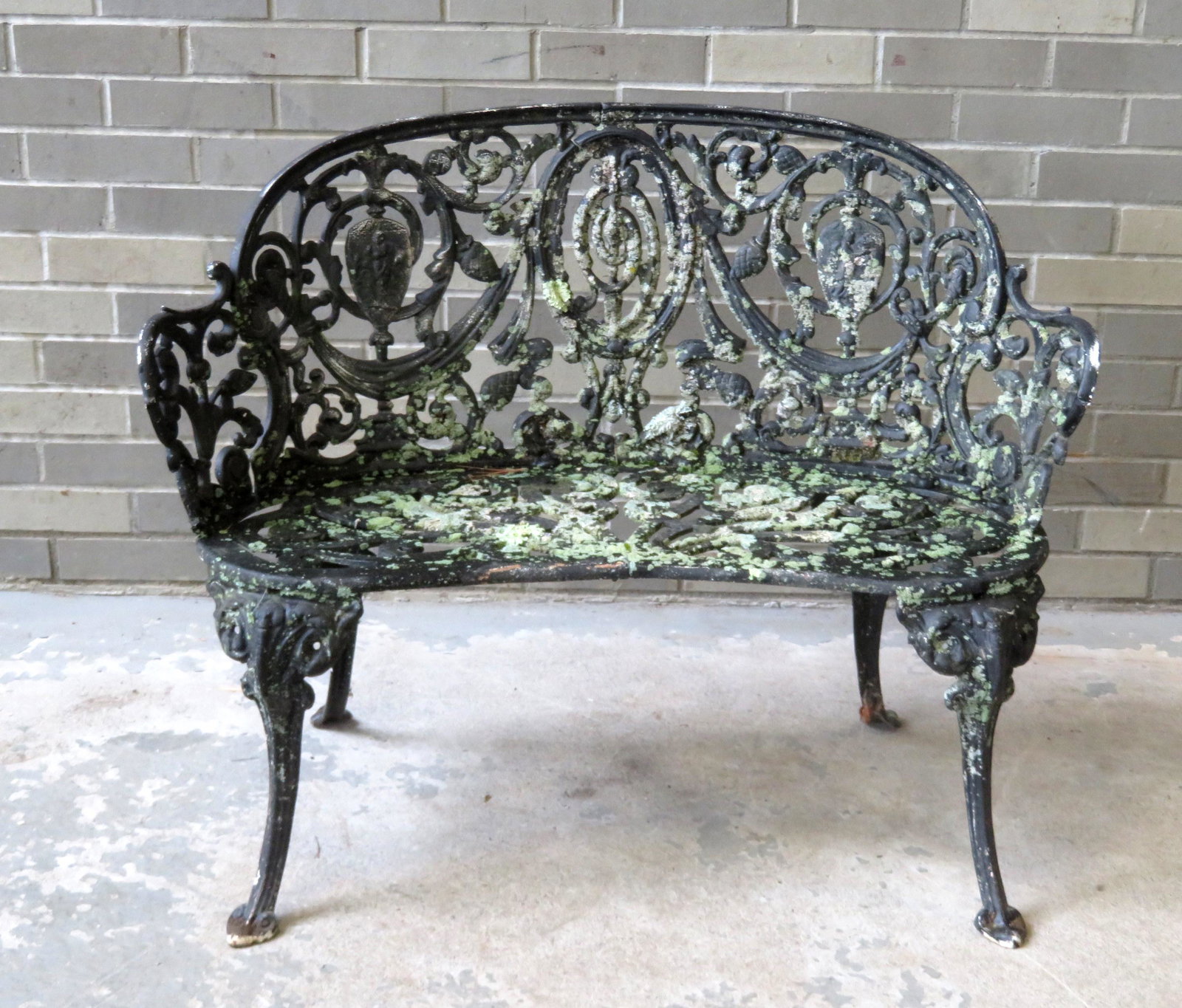 Cast iron classical garden settee decorated with: Cast iron classical garden settee decorated with scrolls and swags, mid 20th century, in old black paint covered with lichen growth. 36"W x 19"D x 28 3/4"H.