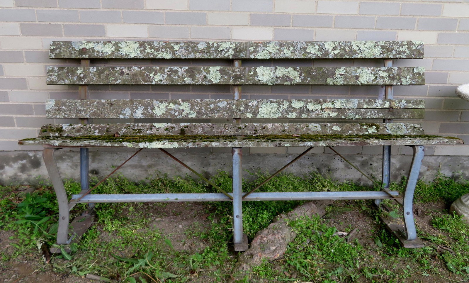 Old wooden slat-back park bench with steel frame. The: Old wooden slat-back park bench with steel frame. The wooden slats with extensive moss and lichen. One plank from the seat has a 6" loss on one end, otherwise the bench is in good condition. Probably 