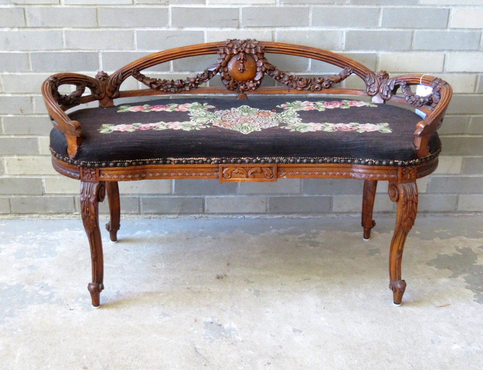 A beautiful profusely carved kidney shaped window bench: A beautiful profusely carved kidney shaped window bench with needlepoint floral seat with an open work triple arched reeded back decorated with flowers and wreaths above exceptional carved floral swag